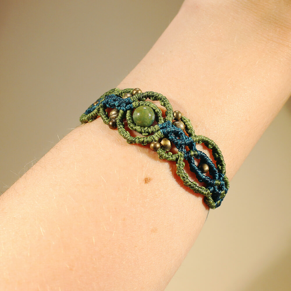 Ett armband i makramé i blått och grönt med en pärla av grön indisk agat