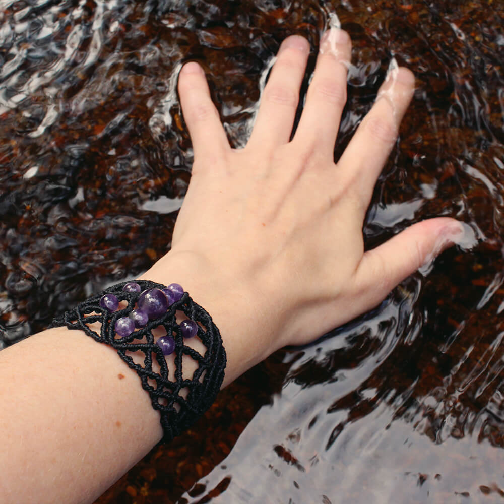 Ett armband med ametist bärs av person som sveper sin hand i en bäck