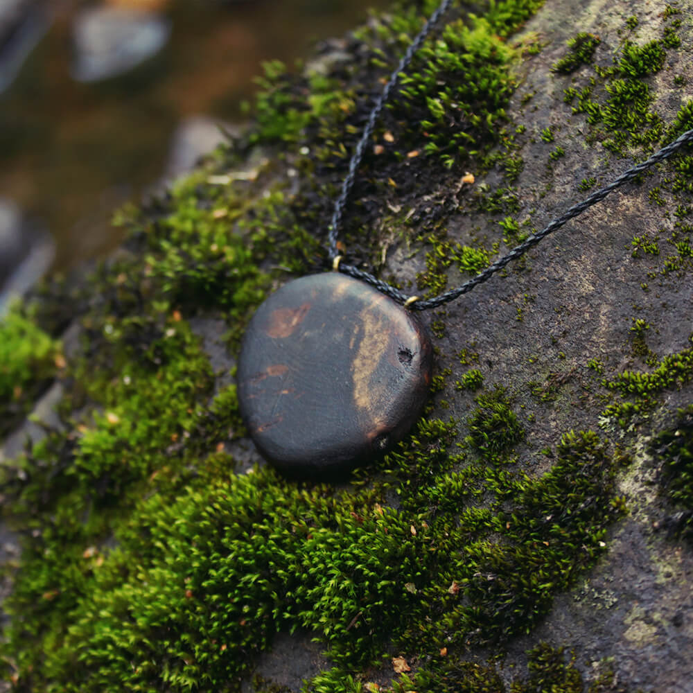 Halsband med runt hänge av asp, liggandes på en sten med mossa