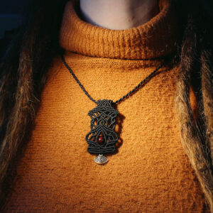 Svart halsband i makramé med ögon, mot orange stickad tröja