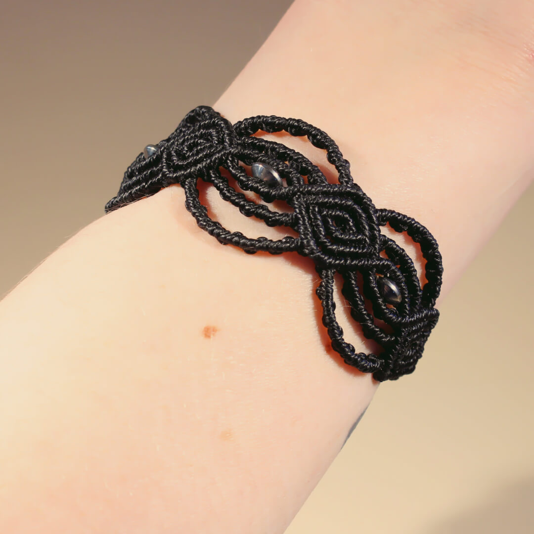 Handled med svart makram&eacute;armband med ovala spiraler och p&auml;rlor i rostfritt st&aring;l