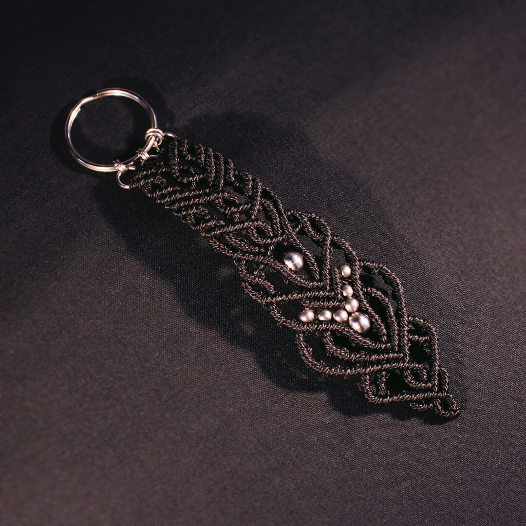 Svart nyckelring i makram&eacute; med p&auml;rlor av rostfritt st&aring;l.